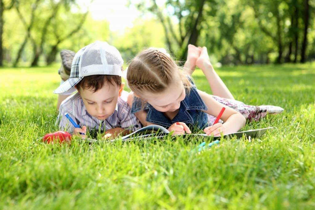 Девочка и мальчик лежат на траве и рисуют